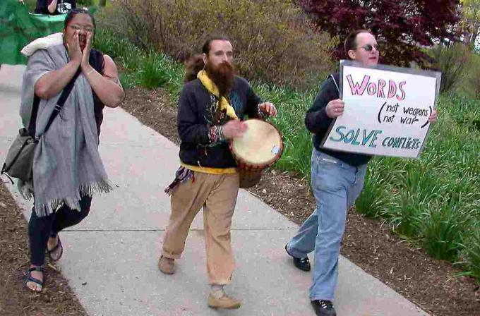 Una mujer grita, un hombre barbudo toca un tambor y otro hombre sostiene un cartel de protesta.