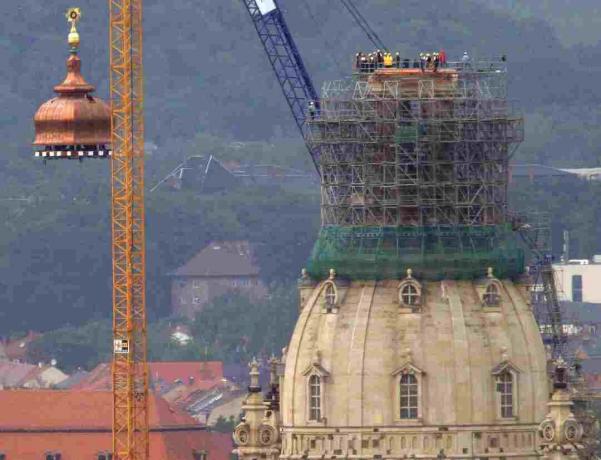 Una grúa levanta la cúpula de cobre y la cruz de oro hasta la cima de la reconstruida Frauenkirche en Dresden, Alemania