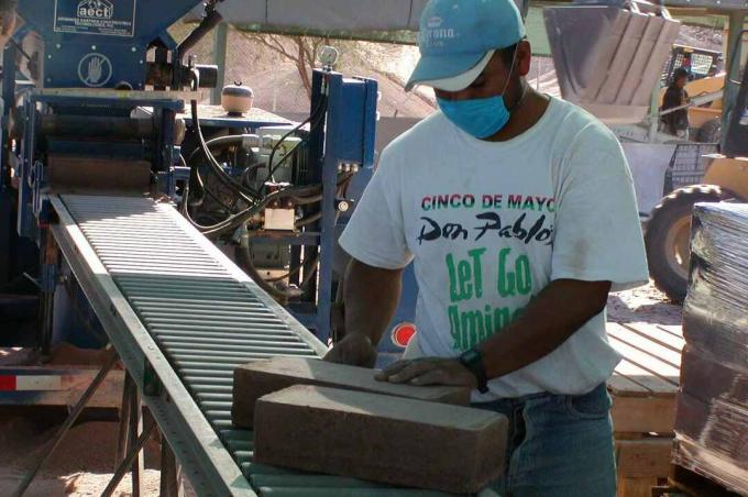 hombre con camiseta, gorra y máscara quirúrgica examina el bloque de tierra en un rodillo transportador