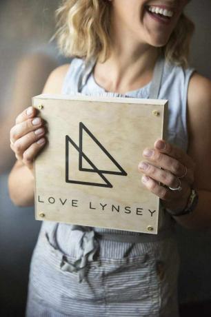 Una mujer sosteniendo una placa de madera con su logo en ella.