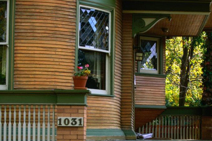Detalle del porche redondeado de la casa, revestimiento de madera natural con molduras verdes, ventanas con plomo de doble hoja, ménsulas decorativas