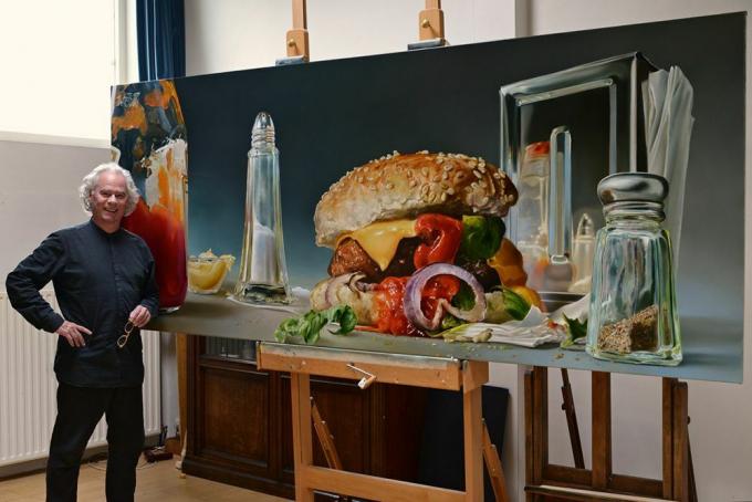 El hombre se encuentra con la imagen de gran tamaño de una hamburguesa y saleros y pimenteros.