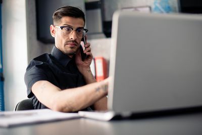 Hombre de gafas en el teléfono con ordenador portátil