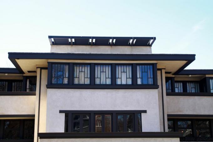 casa de orientación horizontal con paredes de color marrón oscuro, techo plano con enormes voladizos e hileras de ventanas con vidrio emplomado