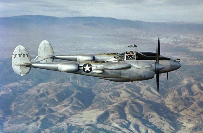 Un luchador P-38 Lightning plateado sobrevolando montañas