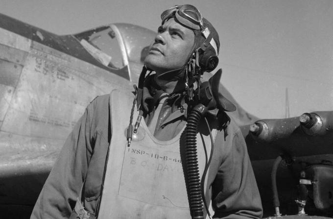 Benjamin O. Davis en traje de vuelo y casco parado frente a un caza Mustang P-51.