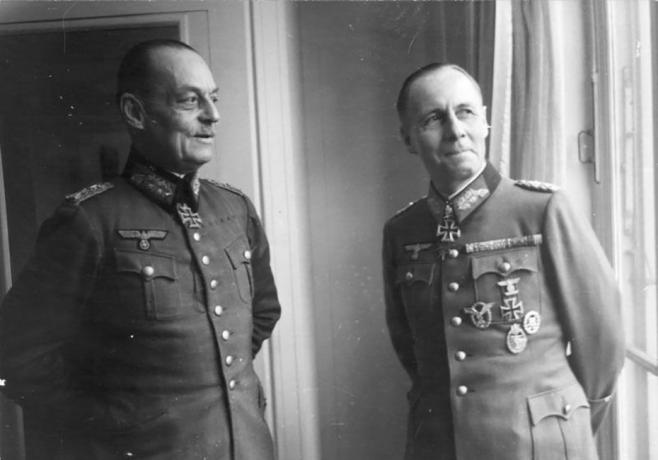 Gerd von Rundstedt y Erwin Rommel con uniformes militares alemanes parados cerca de una ventana.