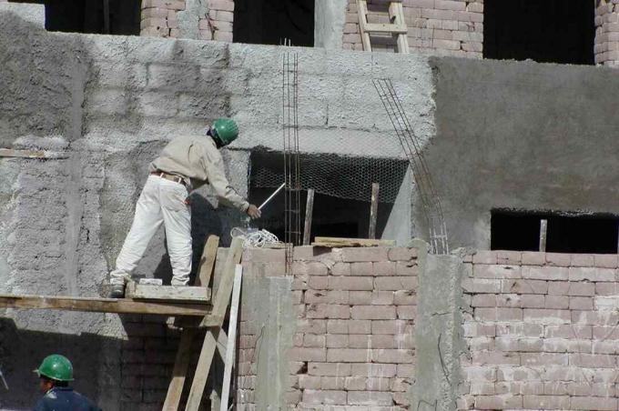 Hombre con casco en andamios trabajando en la pared de bloques de tierra