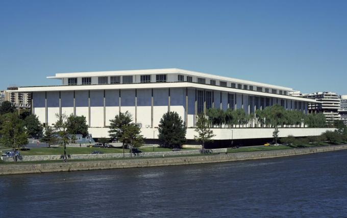 Edificio de poca altura, blanco con postes oscuros distribuidos uniformemente alrededor del lugar.