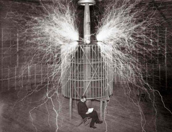 Nikola Tesla sentado en su laboratorio de Colorado Springs junto a su enorme 