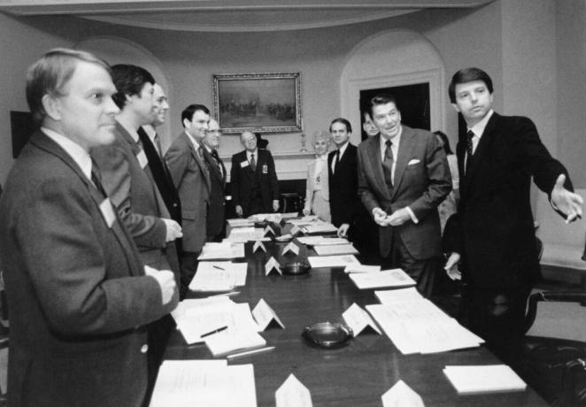 Una imagen en blanco y negro de Ronald Reagan y varios otros hombres de traje alrededor de una larga mesa de conferencias.