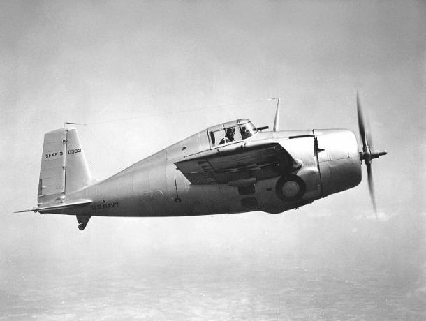 Grumman XF4F-3 Wildcat volando de izquierda a derecha, acabado en aluminio plateado, piloto mirando hacia afuera.