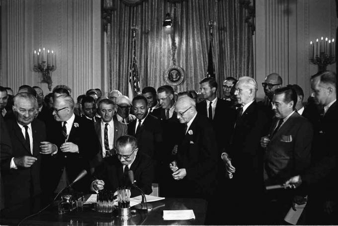 El presidente Lyndon B. Johnson firma la Ley de Derechos Civiles de 1964 mientras Martin Luther King, Jr. y otros observan.
