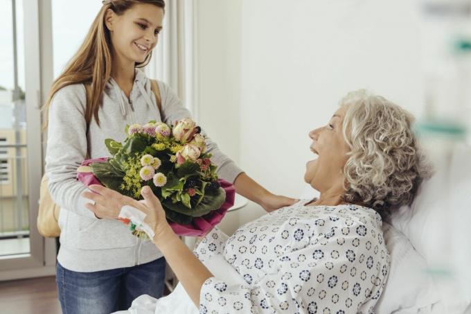 Nieta visitando a la abuela en el hospital, trayendo un ramo de flores