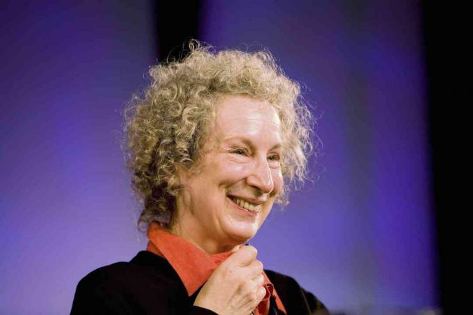 Imagen de Margaret Atwood sonriendo sobre un fondo morado